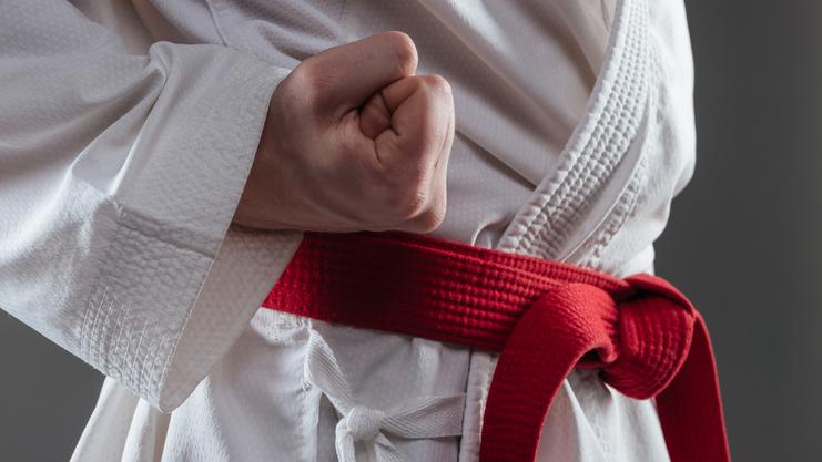 Detailaufnahme einer geballten Faust, die einen weißen Karateanzug mit rotem Gürtel trägt.