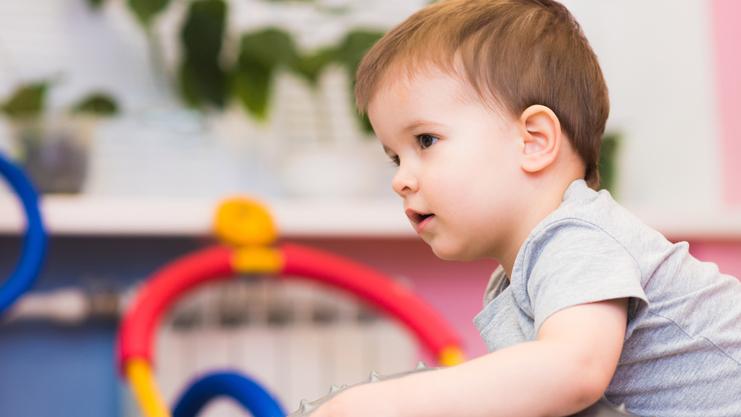Kleines Kind sitzt auf einem großen, stacheligen Gymnastikball in einem bunten Spielzimmer.
