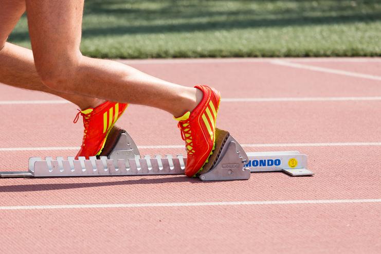 Nahaufnahme eines Fußes in einem roten Laufschuh, der auf einem Startblock auf einer Laufbahn steht.