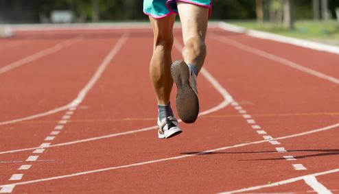 Füße eines Läufers in Sportbekleidung beim Sprinten auf einem roten Tartanbahn.