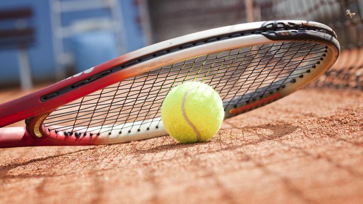 Tennisball liegt auf einem Platz neben einem Tennisracket auf dem Sandboden.