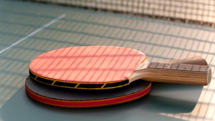 Nahaufnahme von zwei Tischtennisschlägern, einer mit roter und einer mit schwarzer Oberfläche, auf einer Tischtennisplatte.