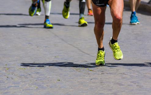Laufende Sportler in bunten Schuhen auf einer steinernen Straße, Fokus auf die Beine und dynamische Bewegung.